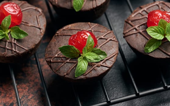 Deliciously rich chocolate brownies garnished with vibrant cherries and mint leaves, resting on a black wire rack.
