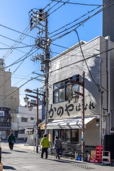People walking on a typical japanese street with messy power lines and restaurant