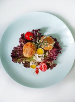 Two juicy meatballs are served on fresh lettuce with halved quail eggs, cherry tomatoes, spices, and herbs