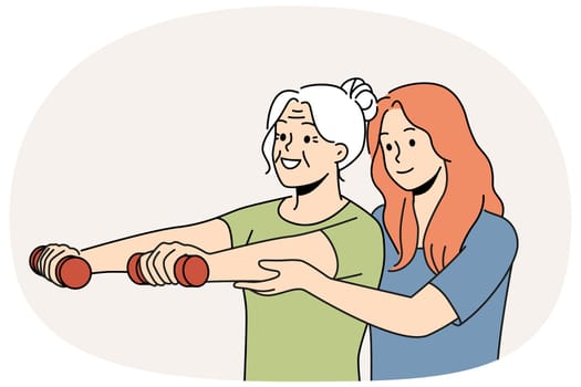 Elderly woman trains with physiotherapist and lifts dumbbells to stay healthy after retirement. Physiotherapist girl helps grandmother go in for sports and do fitness exercises to improve well-being