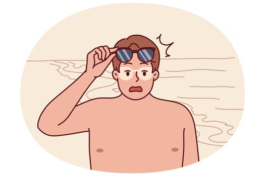 Tanned man takes off sunglasses and screams after getting sunburn relaxing on beach. Funny guy tanned during trip to resort and needs cream to protect against sun rays and ultraviolet radiation