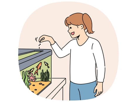 Little girl feeds fish in aquarium and watches underwater pets swimming with pleasure. Happy kid stands near large home aquarium and treats food to sea animals floating among algae