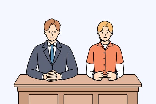 Man lawyer and woman defendant in handcuffs sit at table awaiting verdict from judge. Lawyer defends interests of girl accused of crimes and at risk of receiving prison sentence for breaking law.
