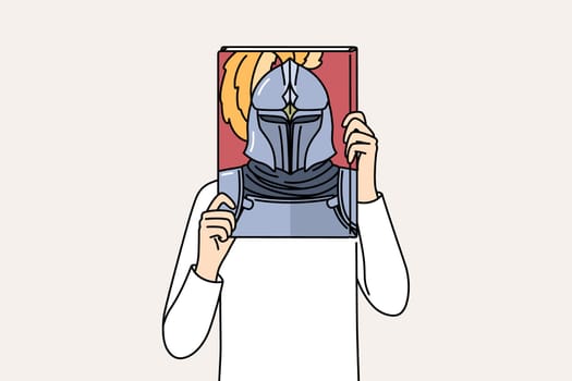 Book with knight on cover in hands of man covering face, reading literature about medieval soldiers. Man pretends to be knight in armor, dreaming of participating in gladiatorial tournaments.
