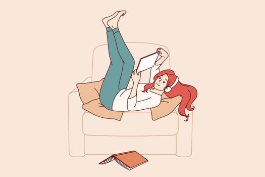 Lazy girl student listens to music lying in chair, distracted from reading textbook to prepare for exams. Lazy young woman enjoying using gadgets, doing idleness after hard day at work.