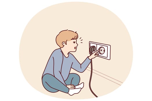 Small boy sticks fingers into socket, playing with electrical equipment and risking electric shock. Preschool child with curiosity pulls fingers to electrical socket and needs attention of parents
