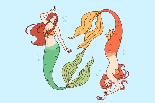 Two mermaids swim deep underwater demonstrating ability to dive to seabed and not breathe for long time. Mermaids from fairy tales or mythical legends, with tails instead of legs and beautiful hair