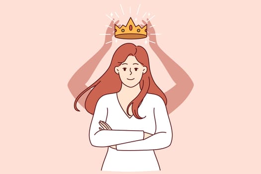 Self-confident woman with crown above head stands with arms crossed in front of chest and looks at screen smiling. Self-confident girl rejoices at gold award for achieving success in career