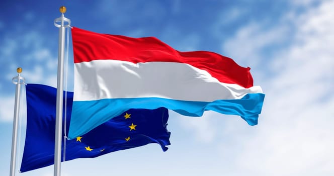 Flags of Luxembourg and the European Union waving in the wind on a clear day. 3d illustration render. Fluttering textile. Selective focus