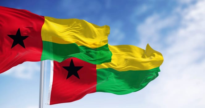 National flags of Guinea-Bissau waving in the wind on a clear day. Vertical red stripe, black star left, yellow and green horizontal stripes right. 3d illustration render. Fluttering fabric