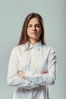 Studio portrait featuring a young businesswoman with arms crossed, exuding seriousness and confidence while showcasing determination and professionalism in a formal white shirt