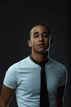 Portrait showcasing a stylish young man in a tie, confidently looking at the camera against a sleek black background. Portrait