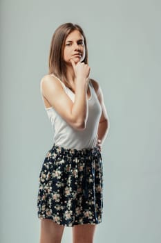 Portrait of a thoughtful young woman touching her chin with her hand, expressing deep thought and contemplation against a neutral gray background