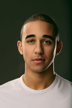Serious young man gazing directly at the camera against a dark background, exuding calm confidence and deep contemplation. Portrait