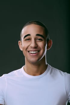 Cheerful young man smiling broadly, showcasing his teeth against a dark background, radiating happiness and confidence in a studio setting. Portrait