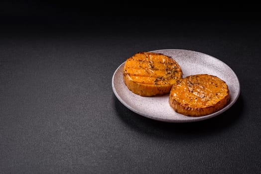 Pumpkin cut into slices and grilled with rosemary and spices on a dark concrete background