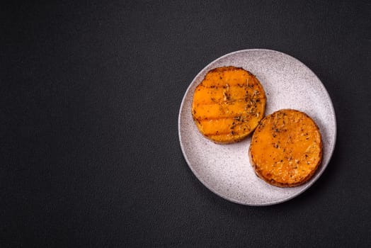 Pumpkin cut into slices and grilled with rosemary and spices on a dark concrete background