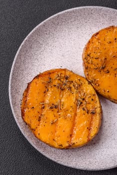 Pumpkin cut into slices and grilled with rosemary and spices on a dark concrete background