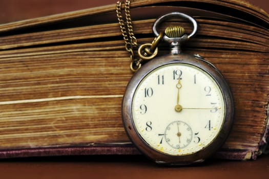 An antique pocket watch leans against an old book with yellowed pages