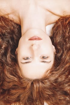 Close-up portrait of a young woman lying down, her long, flowing red hair elegantly framing her serene face, radiating a sense of calm and natural beauty in soft, natural light