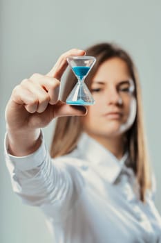 Businesswoman showing an hourglass with blue sand, focusing on the concept of time management, deadlines, and the importance of every second in business