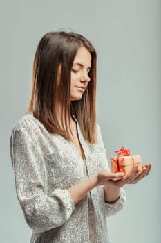 Young woman is holding a small gift in her hands, her eyes closed and a peaceful expression on her face, suggesting feelings of gratitude, happiness, and appreciation for the present moment
