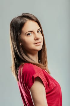 Studio portrait of a beautiful young woman with long brown hair, wearing a red t-shirt, turning her head and looking at the camera with a seductive expression on her face