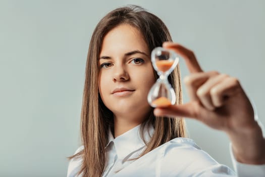 Young businesswoman looking at camera and showing an hourglass, symbolizing time management, efficiency, and the passage of time in a professional context