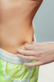 Close-up of a woman pinching her belly fat, emphasizing the ongoing struggle for weight loss and commitment to a healthier lifestyle through fitness and nutrition choices