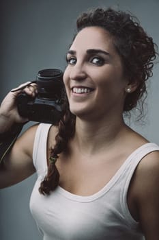 Cheerful young woman photographer holding a dslr camera on her shoulder, radiating passion for photography while capturing moments and expressing her creativity with confidence