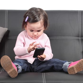 Cute baby browsing in a smartphone sitting on a black couch at home
