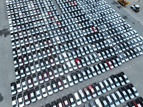Aerial view of new cars stock at factory parking lot. Above view cars parked in a row. Automotive industry. Logistics business. Import or export new cars at warehouse. Big parking lot at port terminal
