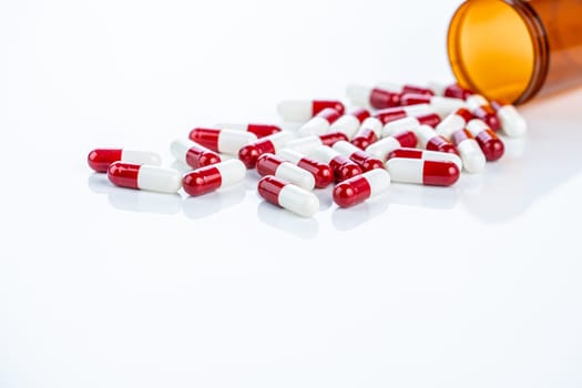 Red and white prescription capsules spilling from a plastic container. Regulated pharmaceutical drugs. Emphasizing safety standards, medication efficacy, and patient well-being in healthcare industry.