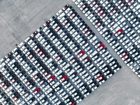 Aerial view of new cars stock at factory parking lot. Above view cars parked in a row. Automotive industry. Logistics business. Import or export new cars at warehouse. Big parking lot at port terminal