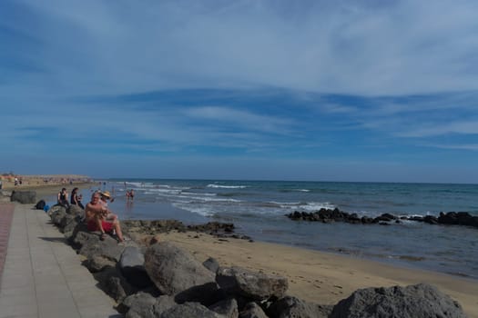 CRAN CANARIA, MELONERAS - NOVEMBER 13, 2019: Cran Canaria, Meloneras, Spain - November 13, 2019: People enjoy the sea view and sit in the sun on the seafront of Meloneras on Gran Canaria, Spain