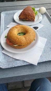 A hearty breakfast spread featuring a sesame seed bagel with tomato and mozzarella, a flaky pastry, and a hard-boiled egg.
