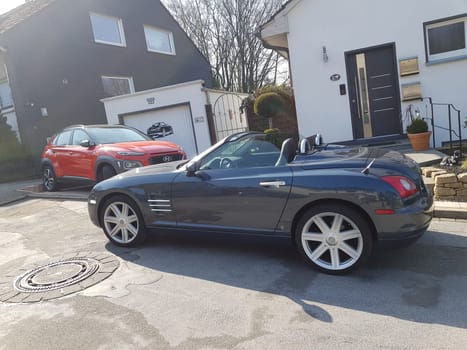 HEILIGENHAUS, NRW, GERMANY - MARCH 28, 2020: Heiligenhaus, Nrw, Germany - March 28, 2020: A Hyundai Kona SUV and Chrysler Crossfire Roadster park in front of a house