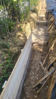 A construction site showing the early stages of foundation work. Exposed earth, wooden formwork, and a level are visible.