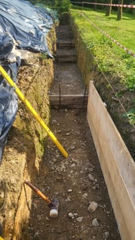 A construction site showing the early stages of foundation work. Exposed earth, wooden formwork, and a level are visible.