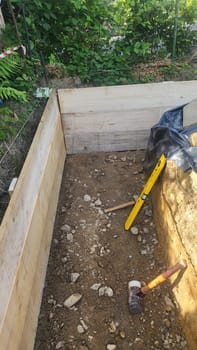 A construction site showing the early stages of foundation work. Exposed earth, wooden formwork, and a level are visible.