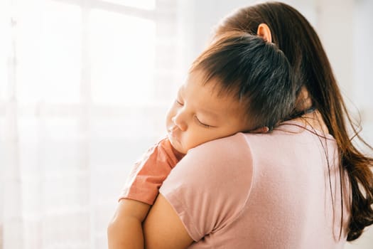 A tender loving biracial mother cradles her small sleeping newborn in her arms sharing an affectionate family moment that exudes the awe of childbirth and the innocence of childhood.