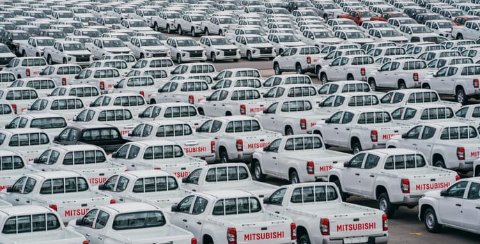 Lamchabang, Thailand - July 02, 2023 bustling car factory distribution center on a cloudy day, new sedans are ready for transport. top view offers glimpse of the crowded parkingan industry in motion.