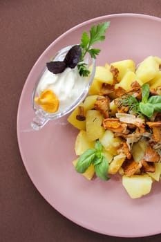 Delicious dish of roasted potatoes with chanterelle mushrooms, herbs, and a side of sour cream, served on a pink plate
