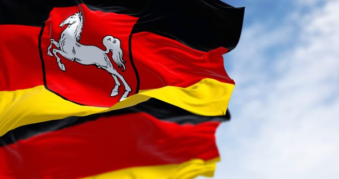 Lower Saxony state flag waving with German flag on a clear day. Black, red and yellow stripes with coat of arms in the center. German state. 3D illustration render. Rippling fabric. Selective focus