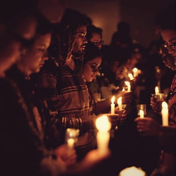 Diverse group of people holding candles in vigil ceremony at night.