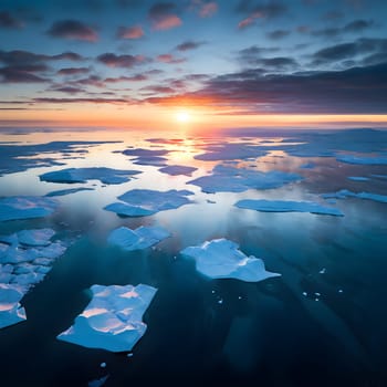 An aerial view of polar icebergs drifting in dark blue waters, sunlight casting turquoise highlights and reflections beneath the ice.