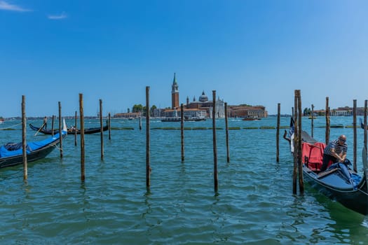 Venice, Italy - July 26, 2024: Gondolas against the San Giorgio island in Venice, Italy. Gondola is the most attractive tourist transport in Venice. Traveling and vacation in sunny Venice.