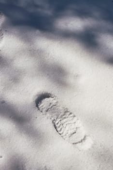 A footprint on virgin snow in sunshine and shadows. Front view, solitary, empty space