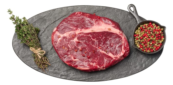 Raw piece of beef and sprig of thyme on black oval board, top view. Isolated background