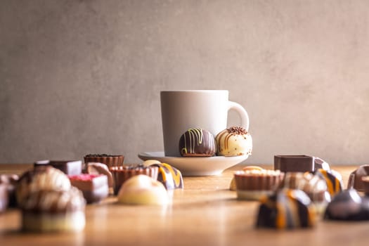 Mix of chocolate pralines and coffee cup on a wooden table.